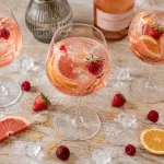 Cocktail vin rosé en verres, glaçons et agrumes sur table en bois