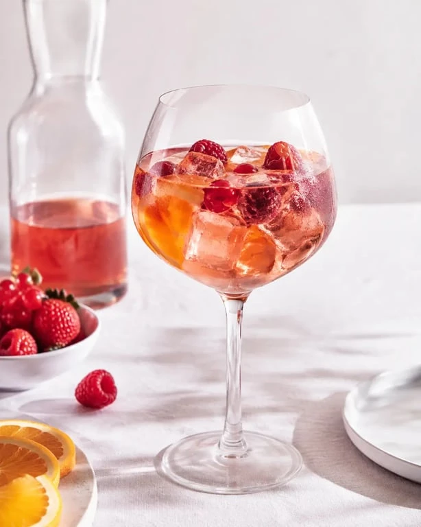 Cocktail vin rosé servi avec glaçons, agrumes et fruits rouges